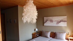 A bedroom with a wooden ceiling, a chandelier, a bed with white linens, a nightstand with a lamp, and a painting on the wall. - Auberge de l'Ange (Haut-Intyamon)