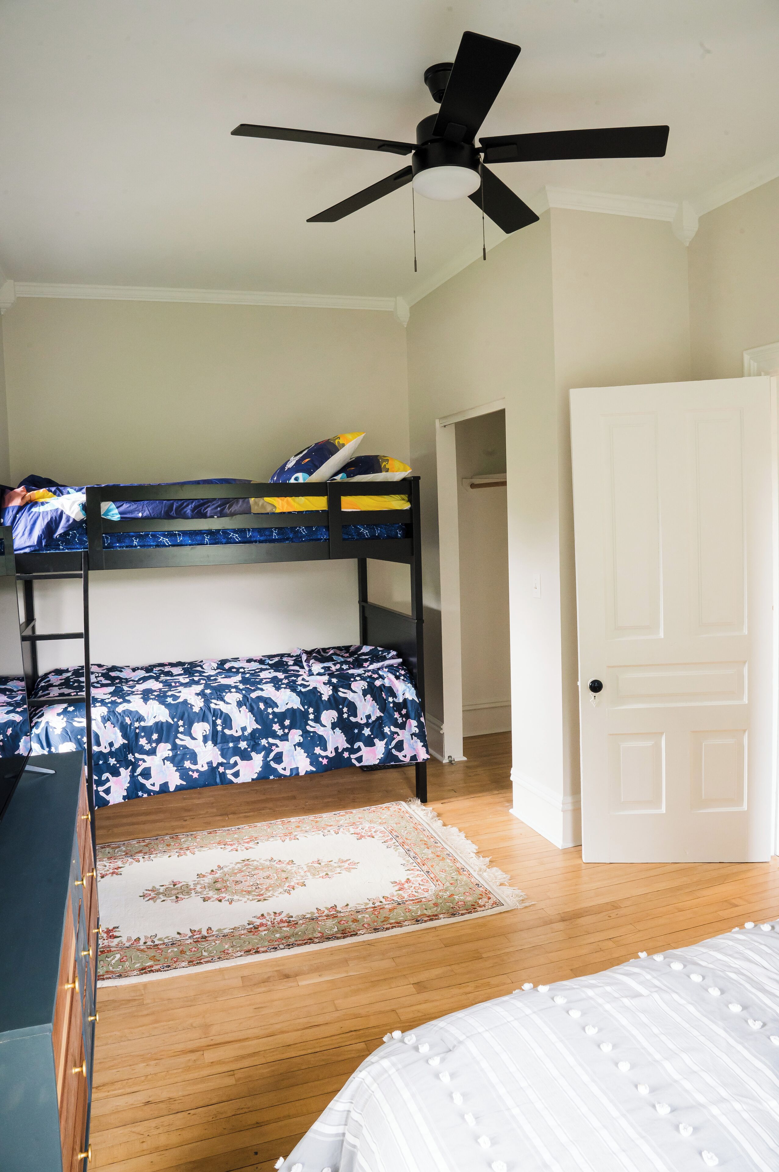 Habitación con literas, ventilador de techo, alfombra estampada y una puerta blanca.