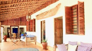 A spacious room with a thatched ceiling, wooden shutters, a sofa with patterned cushions, and a circular rug. - VANILLA BEACH HOUSE - Three Bedroom Villa, Sleeps 6 (Zanzibar)