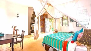 A room with a bed, a table, and a chair. There is a window with curtains and a door. - VANILLA BEACH HOUSE - Three Bedroom Villa, Sleeps 6 (Zanzibar)