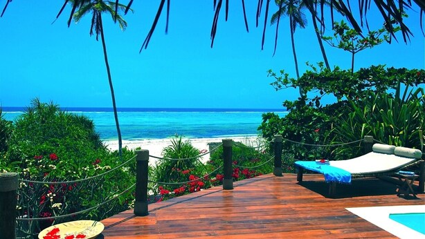 A wooden deck with a pool, lounge chairs, and a view of the beach and ocean. - VANILLA BEACH HOUSE - Three Bedroom Villa, Sleeps 6 (Zanzibar)
