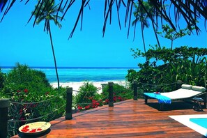 Une terrasse en bois avec une piscine, des chaises longues et une vue sur la plage et l’océan.