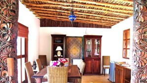 A dining area with a wooden table and wicker chairs, a patterned wall, and a traditional ceiling. - VANILLA BEACH HOUSE - Three Bedroom Villa, Sleeps 6 (Zanzibar)