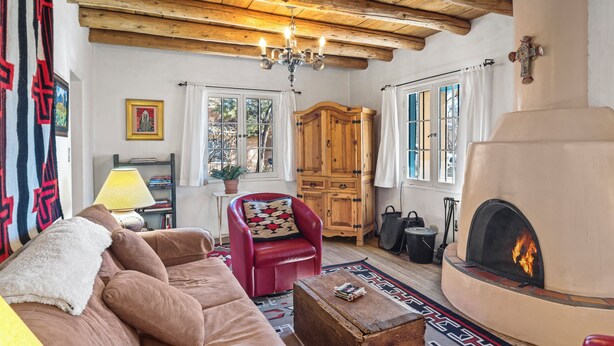 A cozy living room with a fireplace, wooden furniture, and a patterned rug. - Casa Martinez | Historic Santa Fe Charm (Santa Fe)
