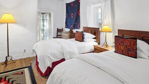 A hotel room with two beds, wooden headboards, a wooden ceiling, a window with white curtains, and a floor lamp. - Casa Martinez | Historic Santa Fe Charm (Santa Fe)