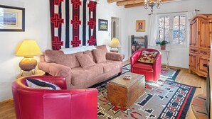 A living room with a sofa, armchair, and ottoman, a wooden cabinet, and a patterned rug. - Casa Martinez | Historic Santa Fe Charm (Santa Fe)