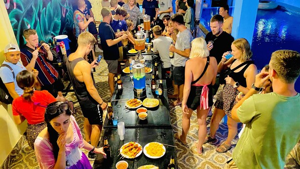A crowded indoor event with a long table filled with food and drinks, surrounded by people. - Vang Vieng Freedom View - Hostel (Vang Vieng)