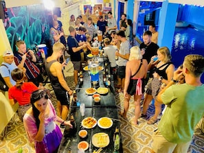 A crowded indoor event with a long table filled with food and drinks, surrounded by people. - Vang Vieng Freedom View - Hostel (Vang Vieng)