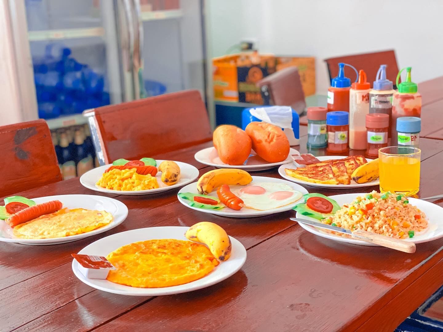 Una mesa de comedor con diversos platos de desayuno, salsas y un vaso de jugo de naranja.