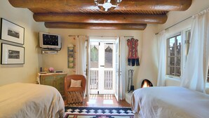 A cozy bedroom with two beds, a television, and a wooden ceiling. - Casa Archuleta | Charming Historic (Santa Fe)