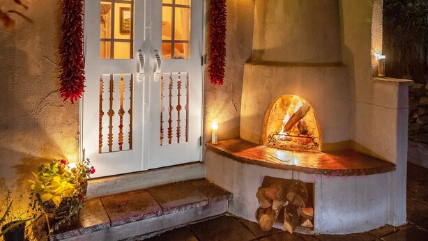 A stone fireplace with a fire, a white door with glass panels, and decorative lights. - Casa Archuleta | Charming Historic (Santa Fe)