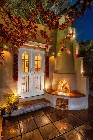 A stone fireplace with a fire, a white door with glass panels, and decorative lights. - Casa Archuleta | Charming Historic (Santa Fe)