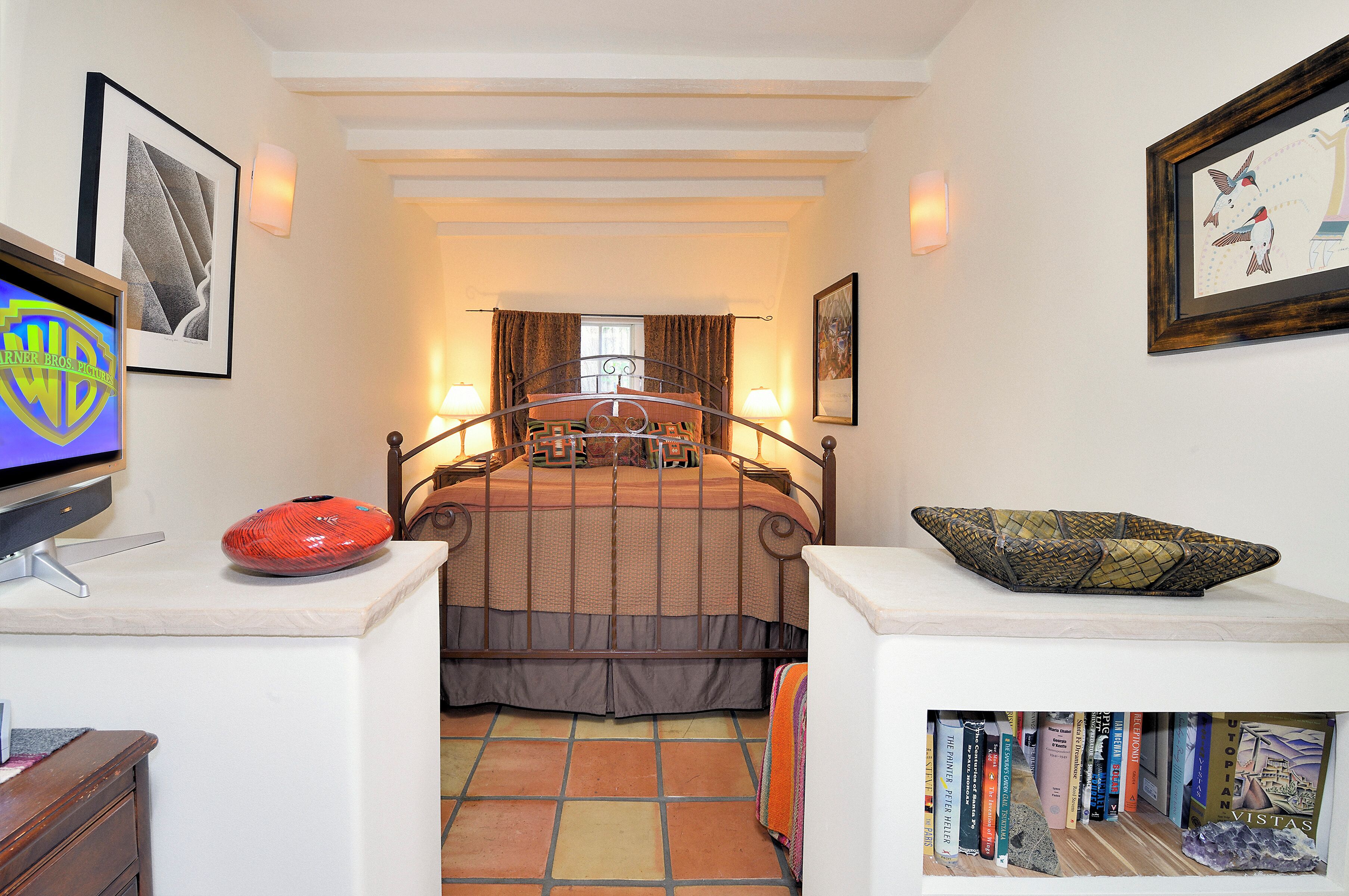 A bedroom with a bed, bedside lamps, a television, a decorative bowl, and a bookshelf.