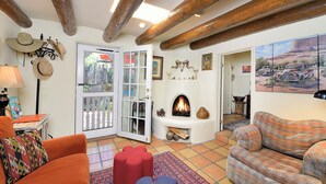 A cozy living room with a fireplace, wooden beams, a sofa, and a door leading to a balcony. - Casa Archuleta | Charming Historic (Santa Fe)