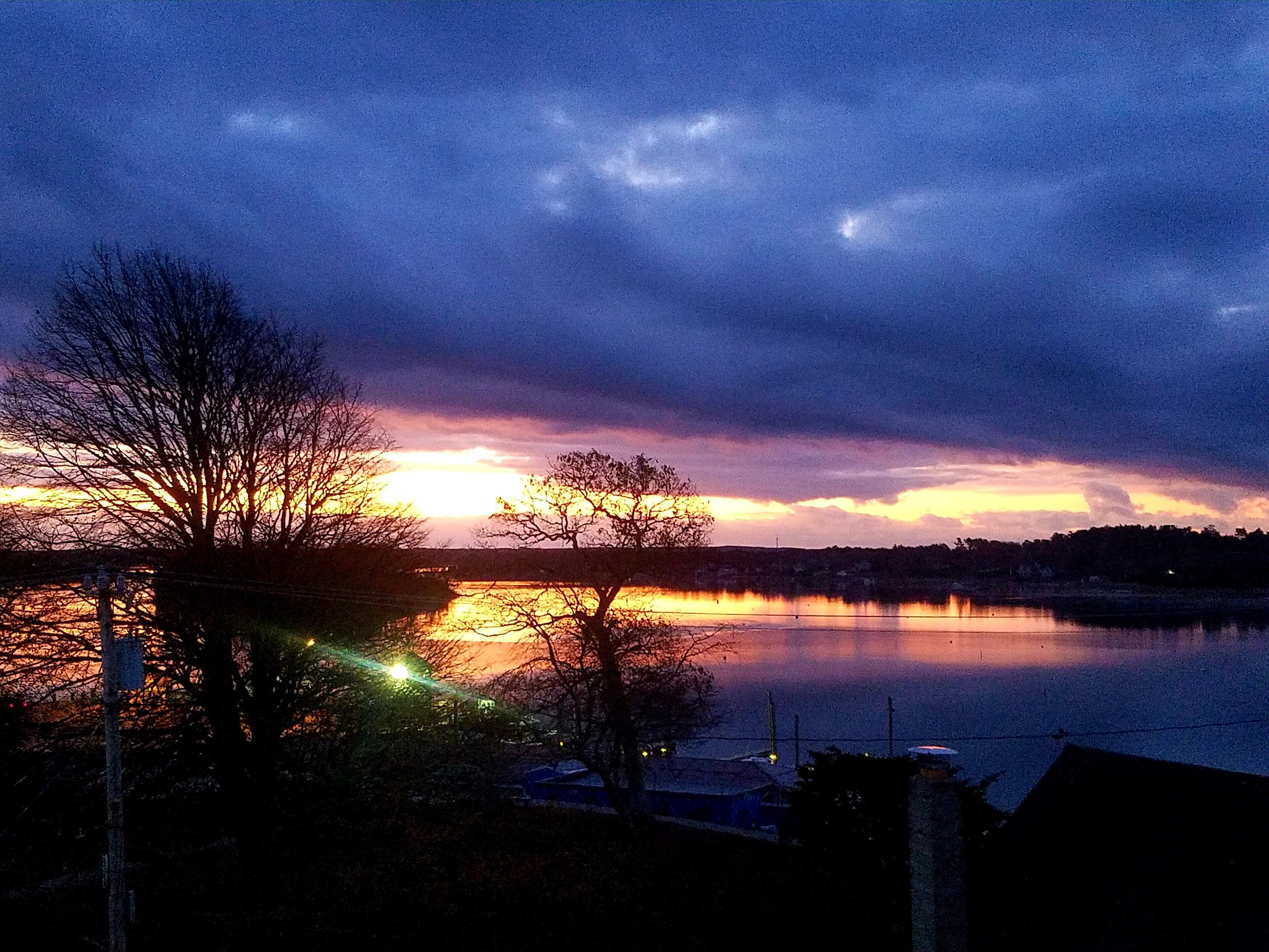 En solnedgång över en stilla sjö, med trädens silhuetter mot himlen.
