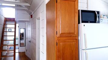 A kitchen with white cabinets, a wooden door, a microwave, and a refrigerator. A wooden ladder is leaning against the wall.