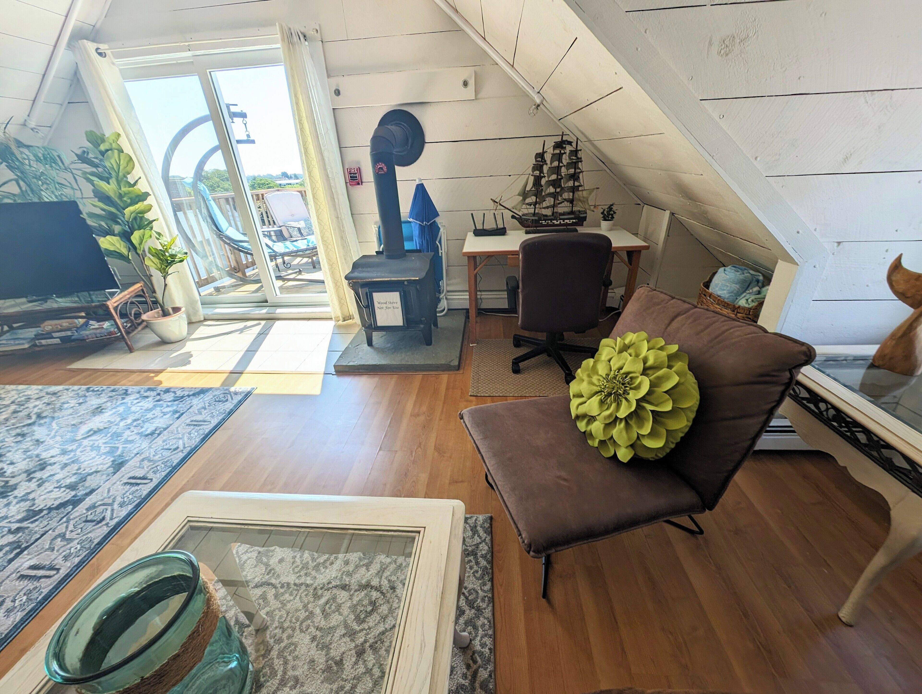 Ein gemütliches Loft mit Holzboden, einem braunen Ledersofa, einem Glastisch und einem Schiffmodell im Regal.