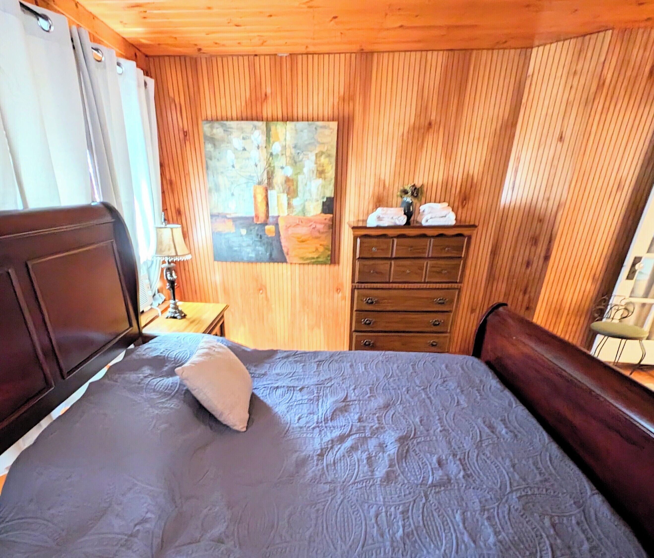 Quarto com painéis de madeira, uma cama, um aparador e um quadro na parede.