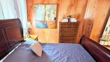 Quarto com painéis de madeira, uma cama, um aparador e um quadro na parede.