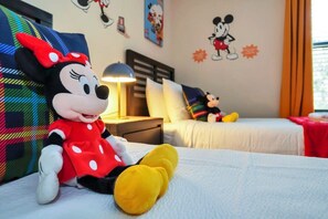 A hotel room with Mickey Mouse and Minnie Mouse plush toys on the bed, a nightstand with a lamp, and Mickey Mouse wall decals. - Charming Townhome | Gated Resort with Pool (Davenport)