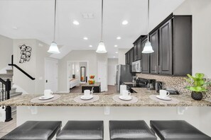 A modern kitchen with granite countertops, dark cabinets, and pendant lighting.