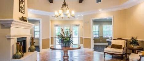 A spacious foyer with a fireplace, a chandelier, and a seating area with chairs and a table.