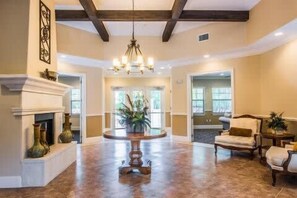A spacious foyer with a fireplace, a chandelier, and a seating area with chairs and a table.