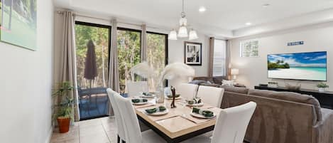 A dining area with a table set for four, a sofa, and a TV on the wall.