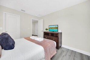 A hotel room with a bed, a dresser, a television on the dresser, and a door leading to another room. - Charming Townhome | Gated Resort with Pool (Davenport)