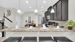 A modern kitchen with granite countertops, dark cabinets, and pendant lighting.