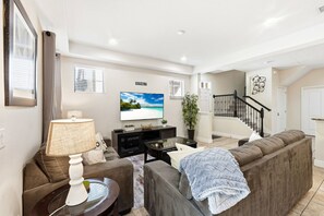 A modern living room with a sofa, a coffee table, a TV, and a staircase leading to another level.