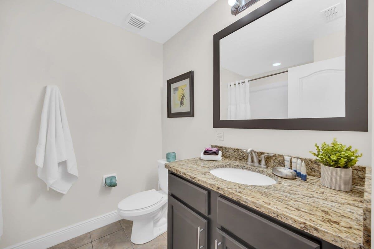 Un bagno con un water bianco, un lavabo con piano in granito, uno specchio grande e un asciugamano appeso al muro.