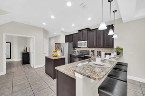 A modern kitchen with dark cabinets, granite countertops, and pendant lighting. - Charming Townhome | Gated Resort with Pool (Davenport)