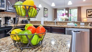 A kitchen with a fruit basket containing apples and oranges on a granite countertop.