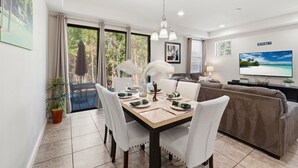 A dining area with a table set for four, a sofa, and a TV on the wall.