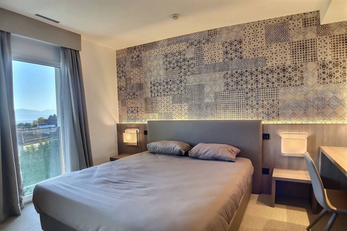 Habitación de hotel con una cama grande, dos mesitas de noche con lámparas, un escritorio y vistas a la ciudad.