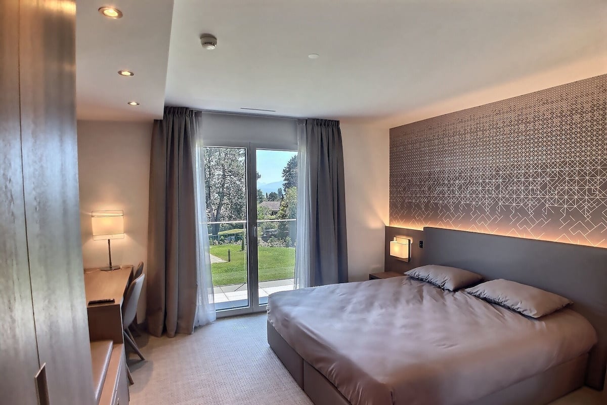 Un hotel moderno con una cama grande, un escritorio con lámpara y vistas al exterior a través de un ventanal corredero.