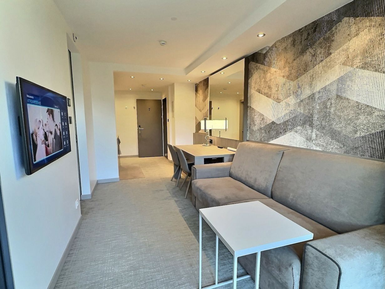 A modern hotel room with a sofa, a small table, a desk with a lamp, and a large abstract wall mural.