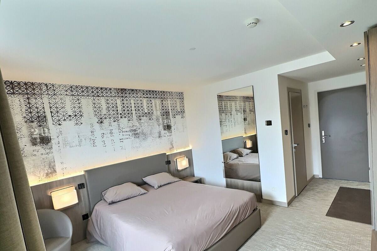 Habitación de hotel moderna con una cama grande, lámparas de noche, un tapiz estampado y una puerta que da a otra habitación.