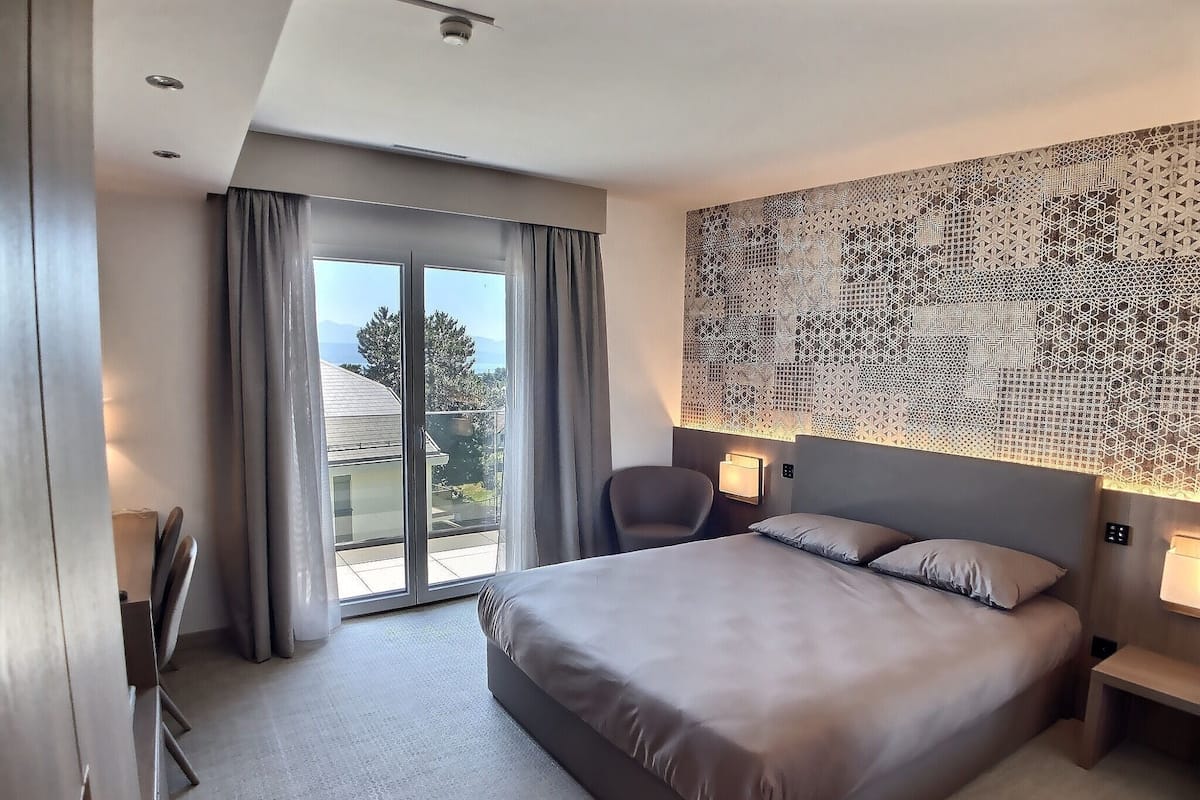 Habitación de hotel con una cama grande, una silla, un escritorio y vistas al exterior a través de una puerta corredera.