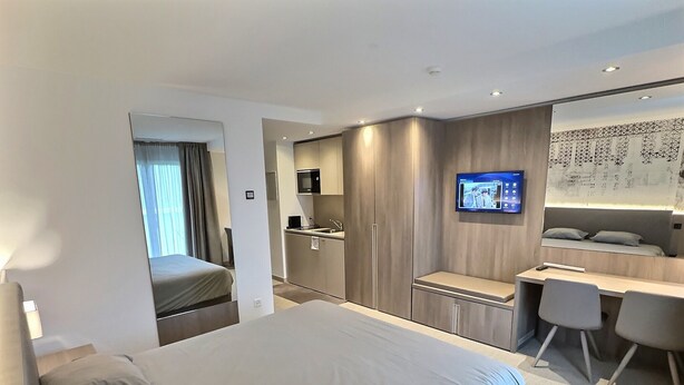 A modern hotel room with a large bed, a desk, a TV, and a wardrobe.