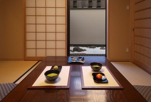 A traditional Japanese room with tatami flooring, a low table with two bowls of food, and a view of a snowy landscape through a sliding door.