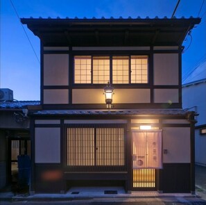 A traditional Japanese building with a tiled roof, a lantern above the entrance, and a sliding door with a sign.
