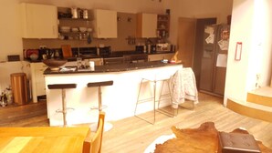 Una cucina con isola centrale, sgabelli da bar, frigorifero e pavimento in legno.