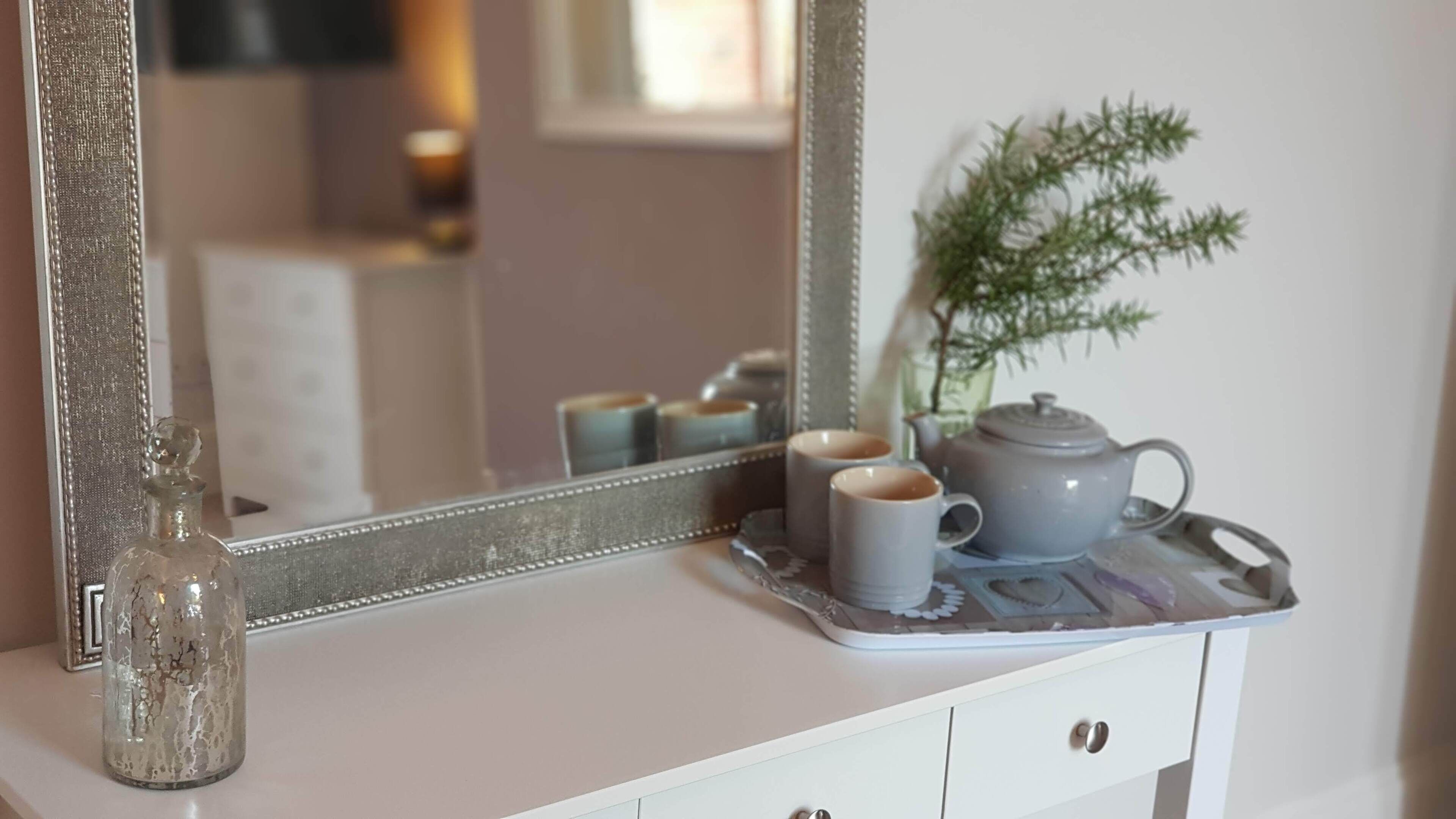Ein Badezimmer-Waschtisch mit Spiegel, einer Glasflasche, zwei Tassen und einem Teekännchen auf einem Tablett.