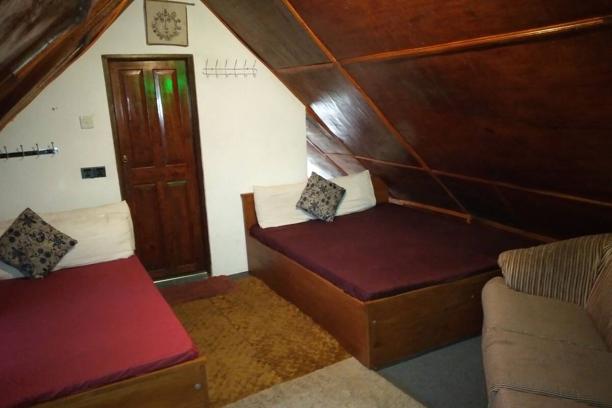 Une petite chambre mansardée, chaleureuse et accueillante, avec deux lits en bois, une porte en bois et un plafond en pente.
