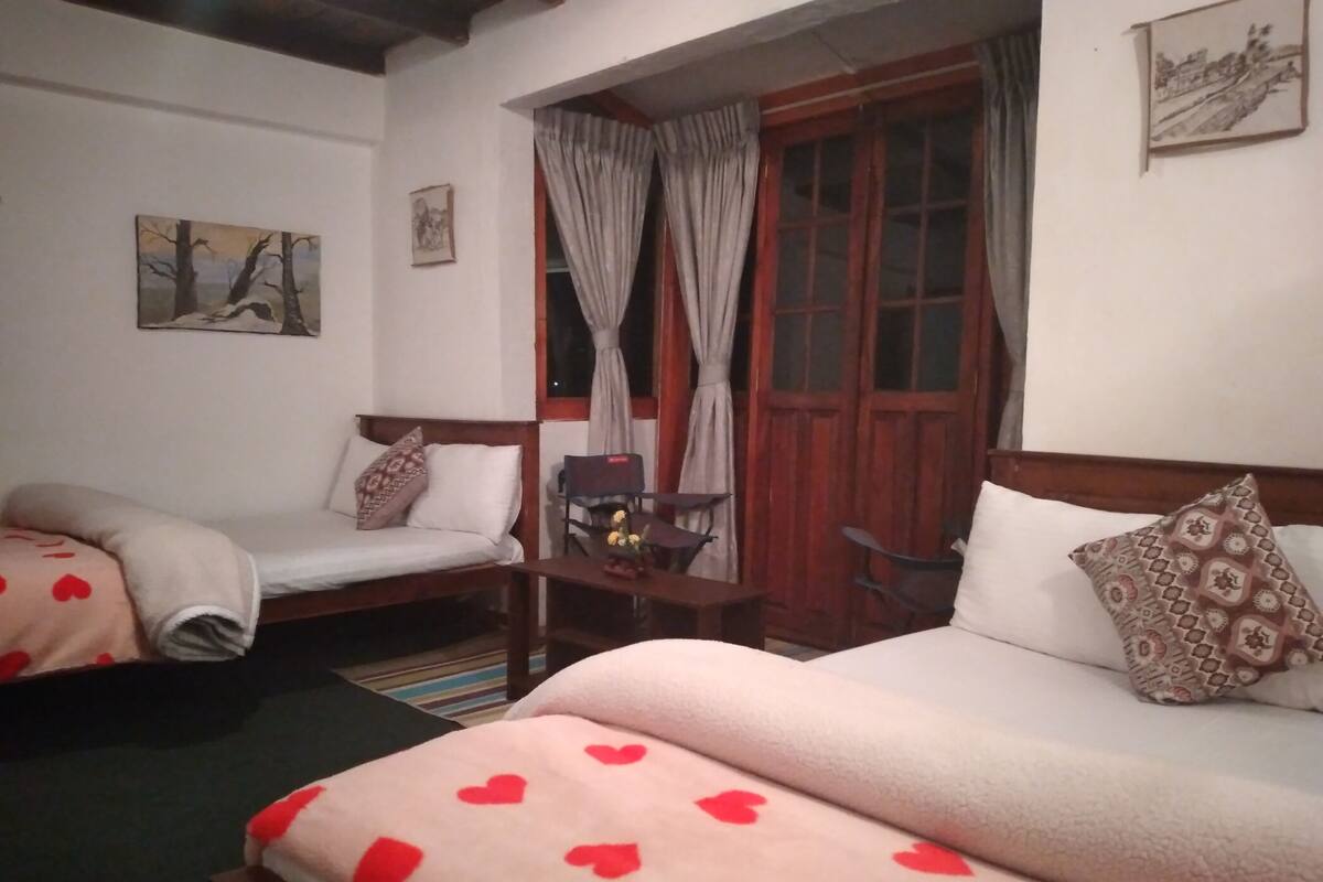 Une chambre d’hôtel avec deux lits, une tête de lit en bois, une petite table avec un vase et une fenêtre avec des rideaux.