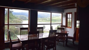 A dining area with a table and chairs, large windows with a view of a lake and mountains, wooden ceiling beams, and a sign on the wall. - Eco Creations Nuwaraeliya (Nuwara Eliya)
