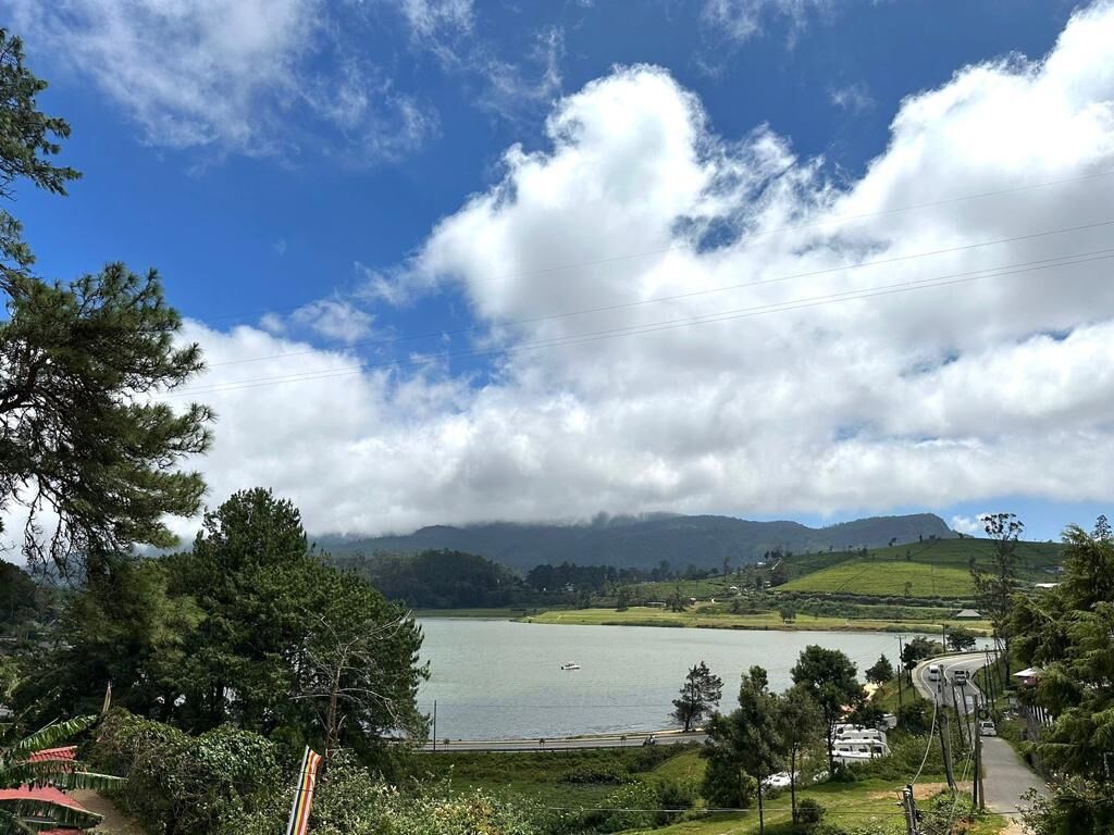 A lake with a road and buildings in the foreground, surrounded by hills and trees.