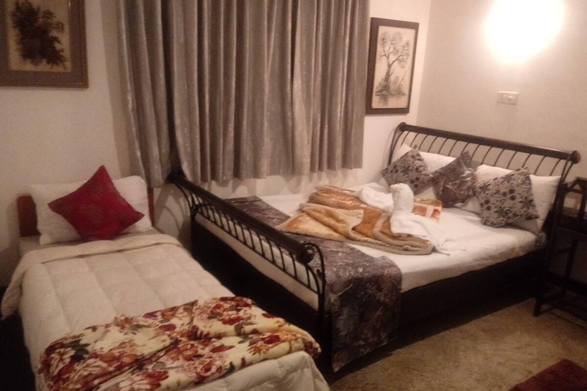 Une chambre avec deux lits simples, une table de chevet, une commode et une fenêtre avec des rideaux.